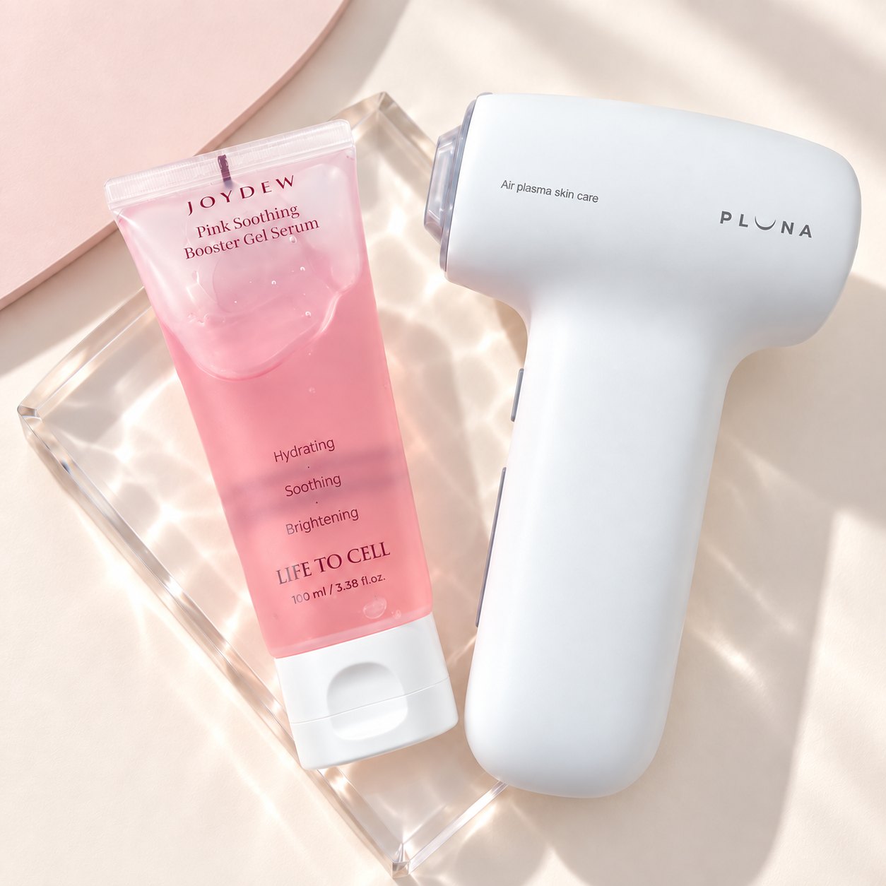 JOYDEW Pink Soothing Booster Gel Serum beside the PLUNA device on a glass tray